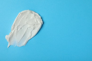 Photo of Smear of delicious cream cheese on light blue background, top view. Space for text