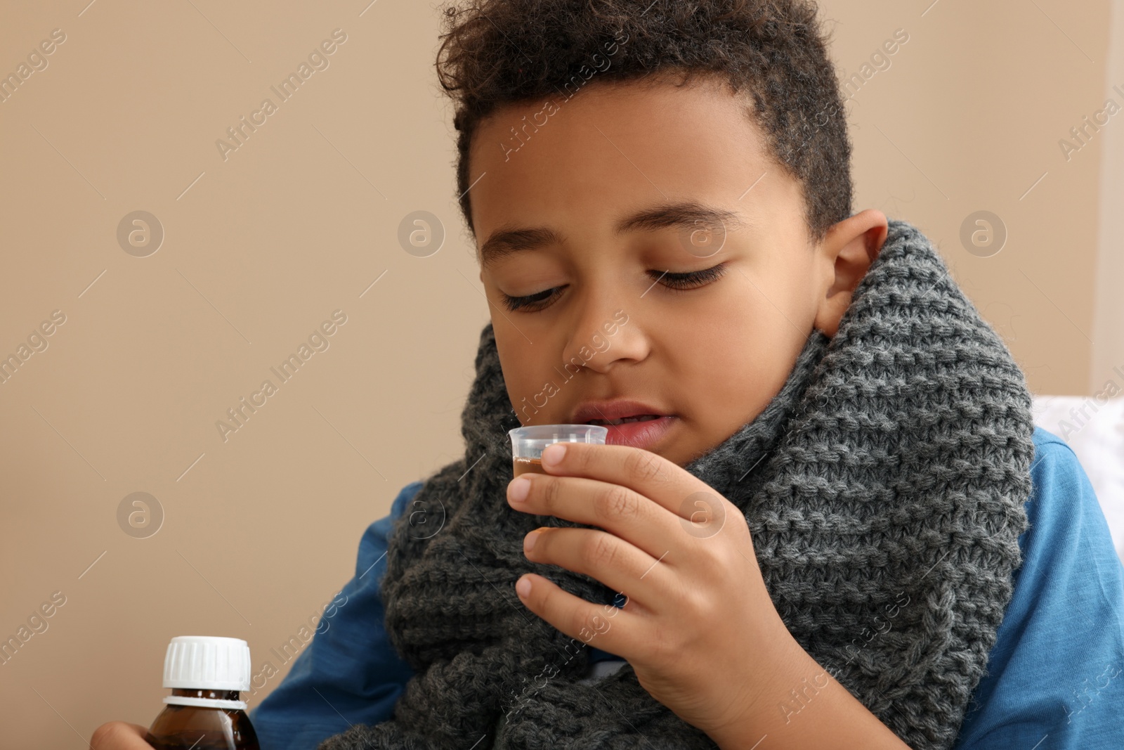 Photo of African-American boy taking cough syrup on bed at home. Cold medicine