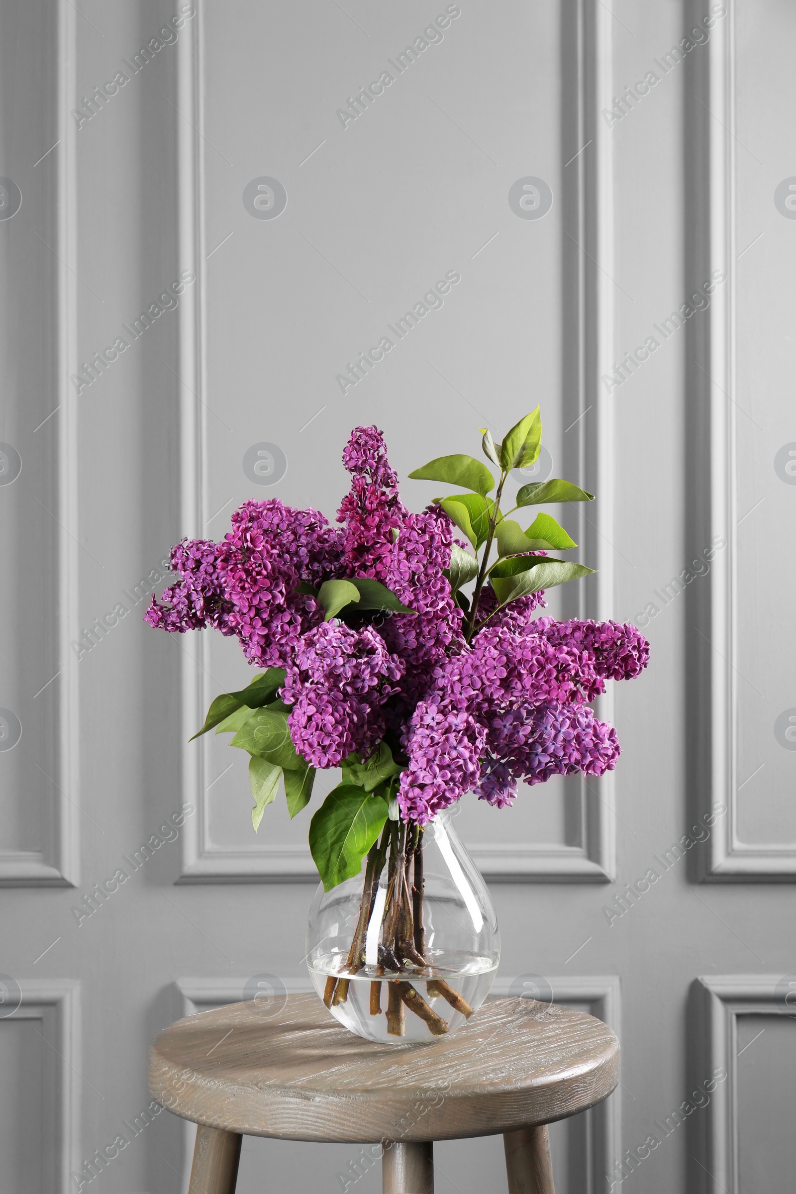 Photo of Beautiful lilac flowers in vase on wooden table near light wall