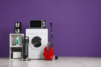 Photo of Set of different home appliances with vacuum cleaner on purple background indoors. Space for text