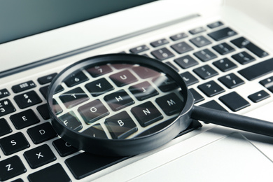 Photo of Magnifying glass on keyboard of modern laptop, closeup. Search concept