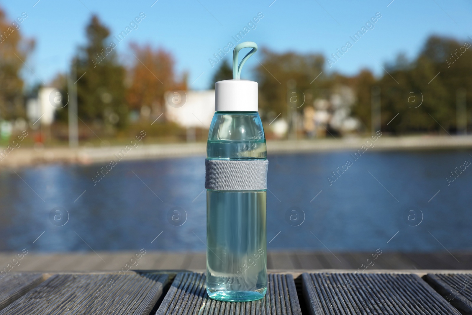 Photo of Glass bottle with water on wooden pier near river outdoors