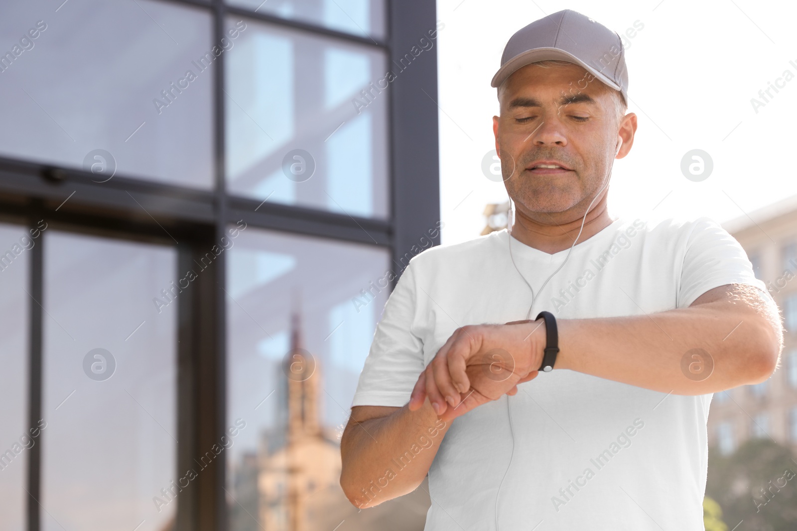 Photo of Handsome mature man looking at fitness tracker on street. Healthy lifestyle