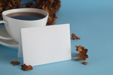 Dried hortensia flowers, sheet of paper and cup with coffee on light blue background. Space for text