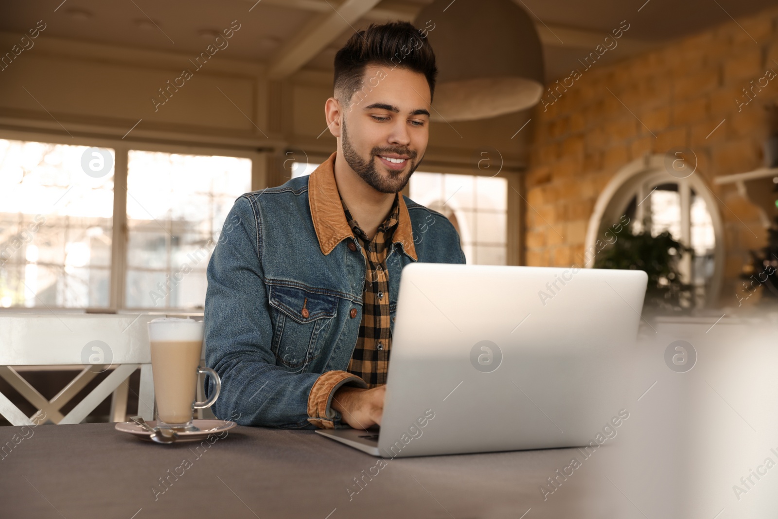 Photo of Young blogger working with laptop at table in cafe