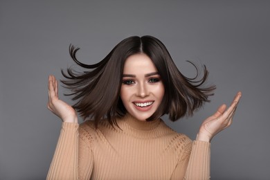 Portrait of pretty young woman with brown hair smiling on grey background