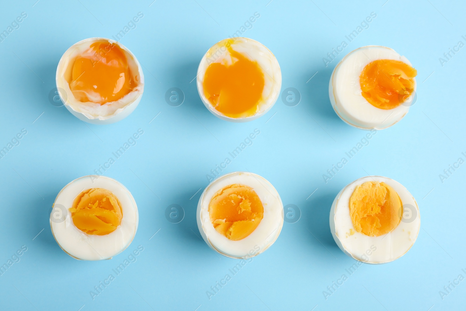 Photo of Different readiness stages of boiled chicken eggs on light blue background, flat lay