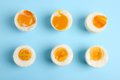 Photo of Different readiness stages of boiled chicken eggs on light blue background, flat lay