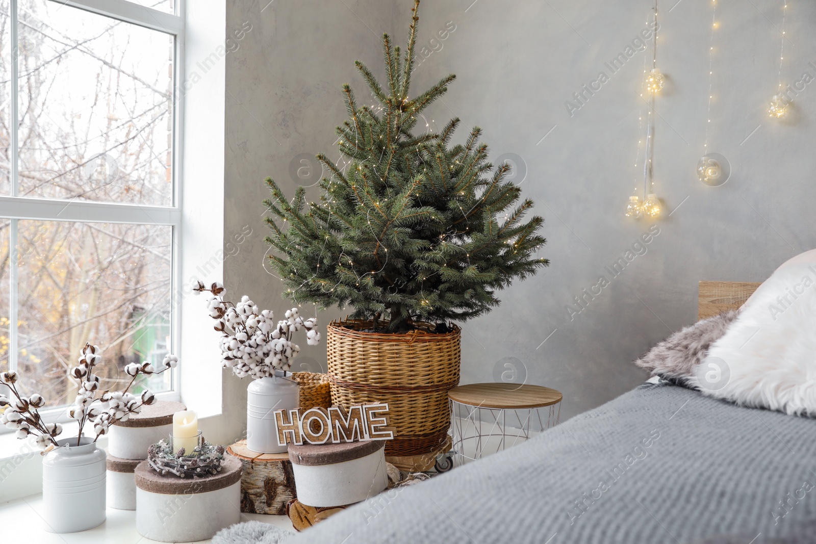 Photo of Little Christmas tree with fairy lights in bedroom interior