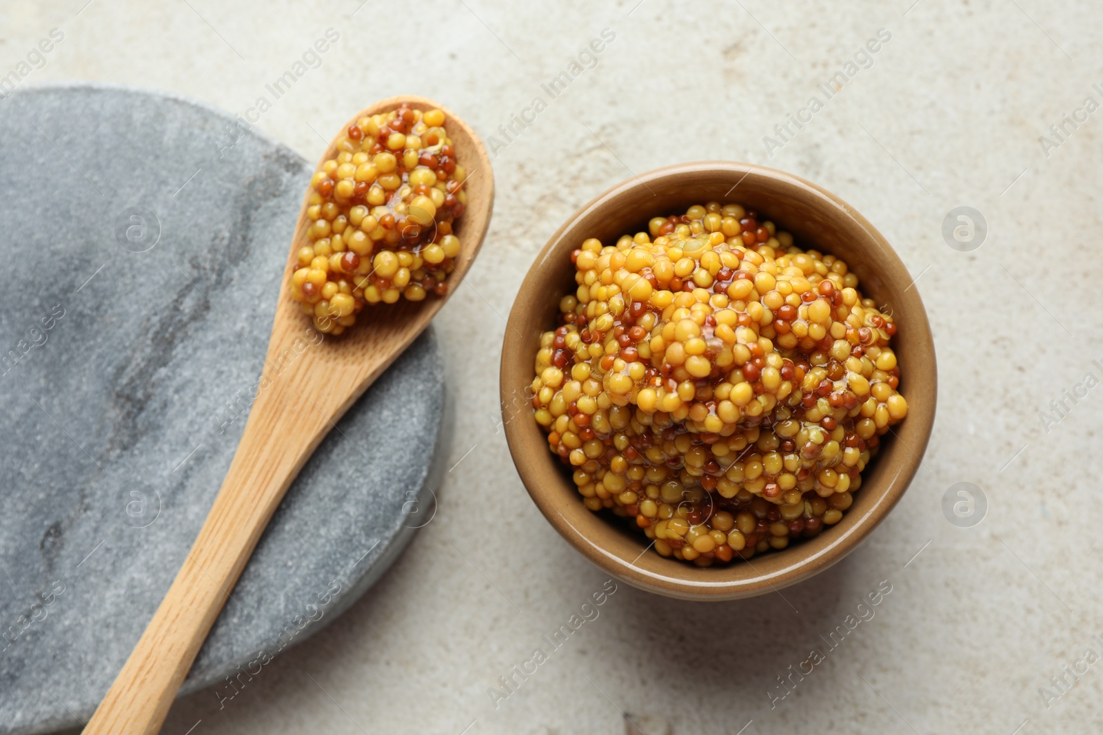 Photo of Bowl and spoon with whole grain mustard on light table, flat lay