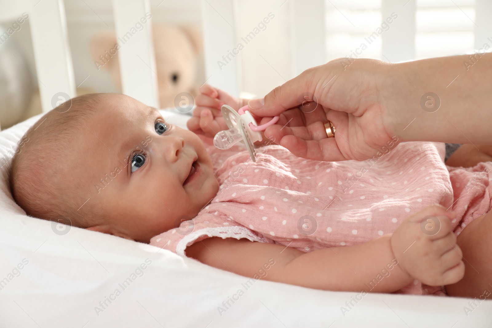 Photo of Mother giving pacifier to cute little baby in soft crib, closeup