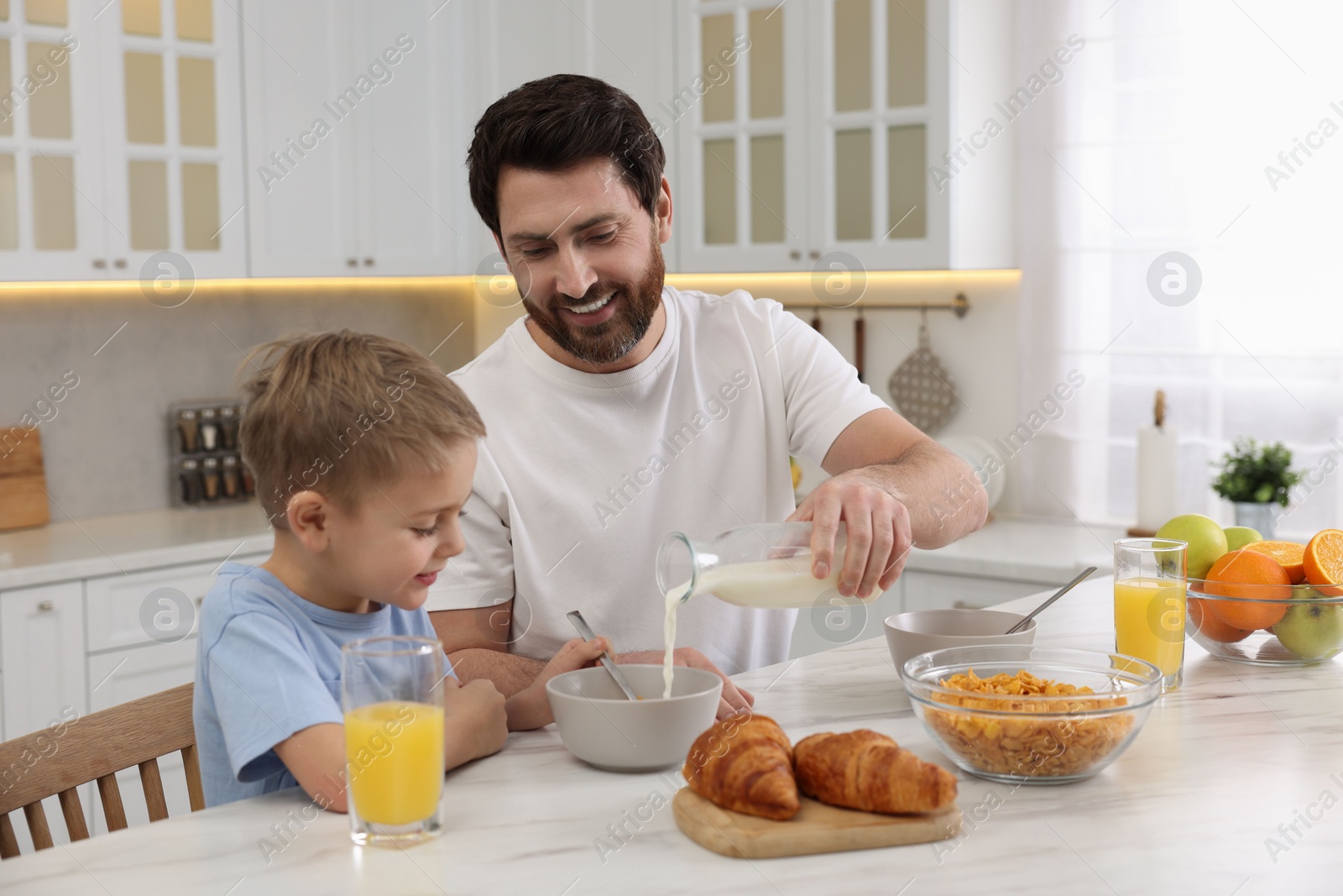 Photo of Father and his cute little son having breakfast at table in kitchen