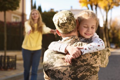 Daughter hugging her father in Ukrainian military uniform on city street. Family reunion