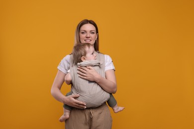 Mother holding her child in sling (baby carrier) on orange background