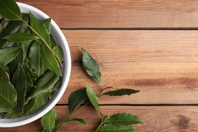 Photo of Aromatic fresh bay leaves and bowl on wooden table, flat lay. Space for text