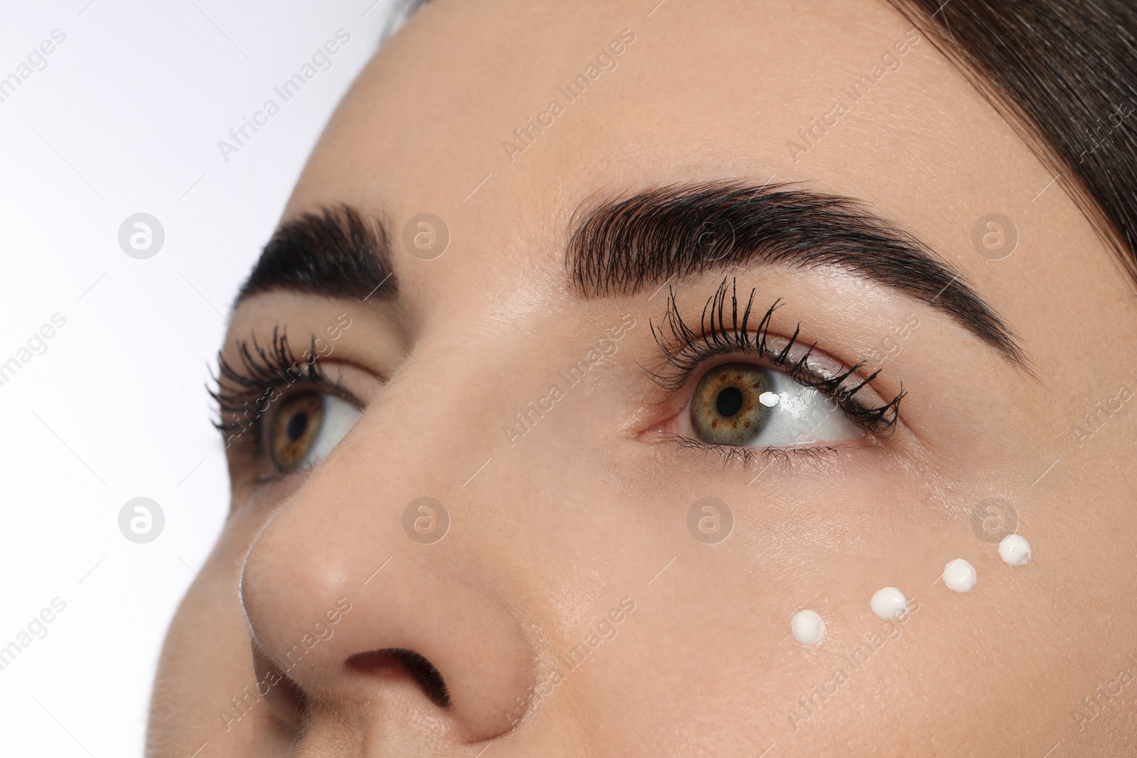 Photo of Woman with cosmetic product around eye on white background, closeup. Skin care