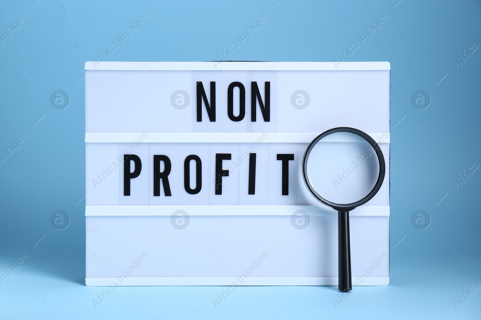 Photo of Lightbox with phrase Non Profit and magnifying glass on light blue background