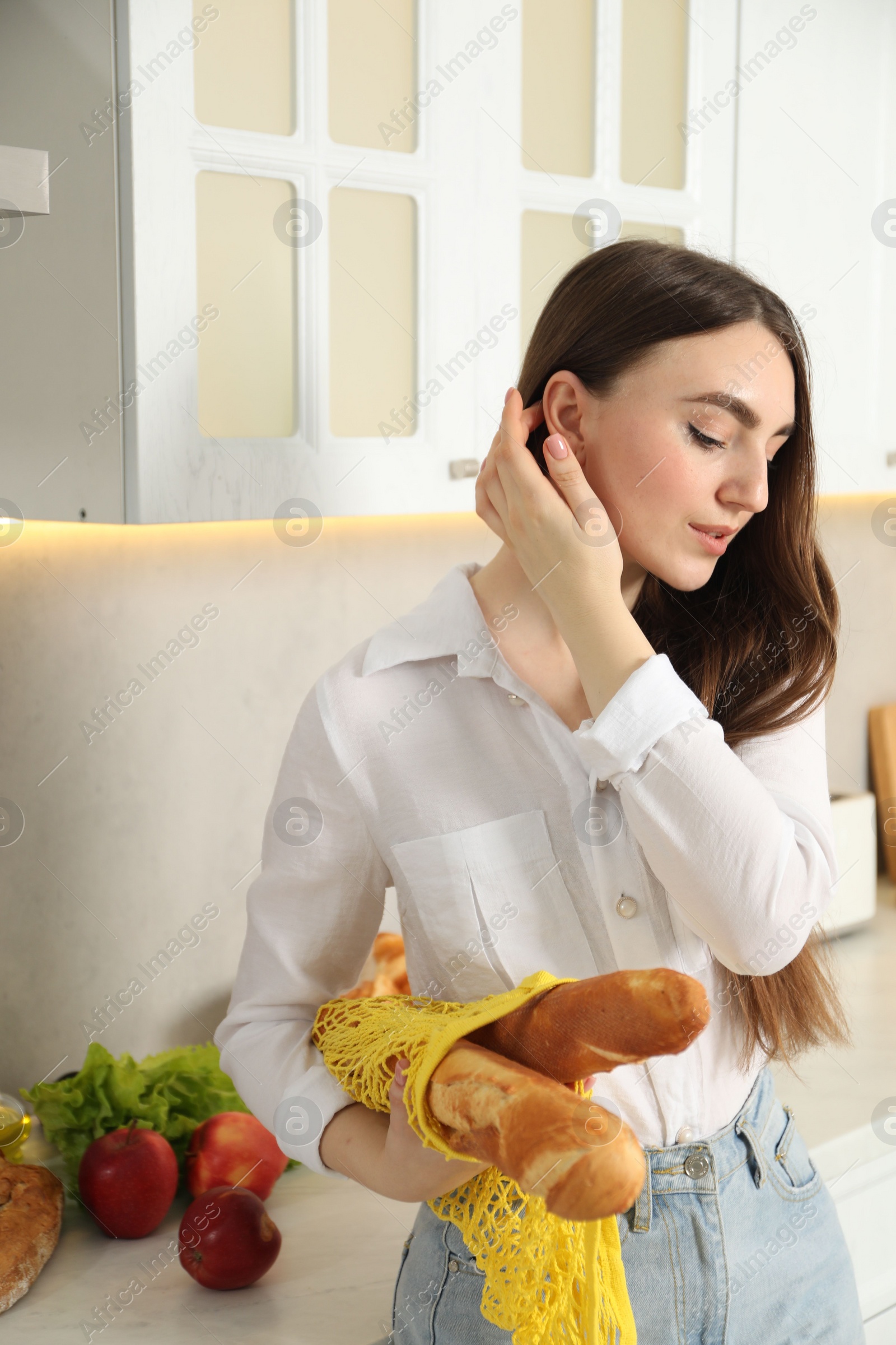 Photo of Woman with string bag of baguettes in kitchen