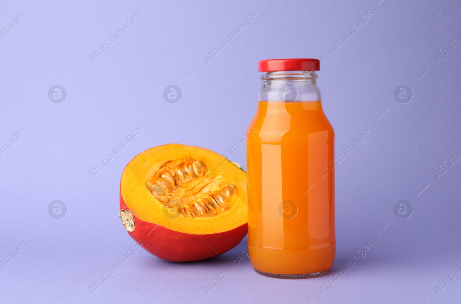 Photo of Tasty pumpkin juice in glass bottle and cut pumpkin on lavender color background
