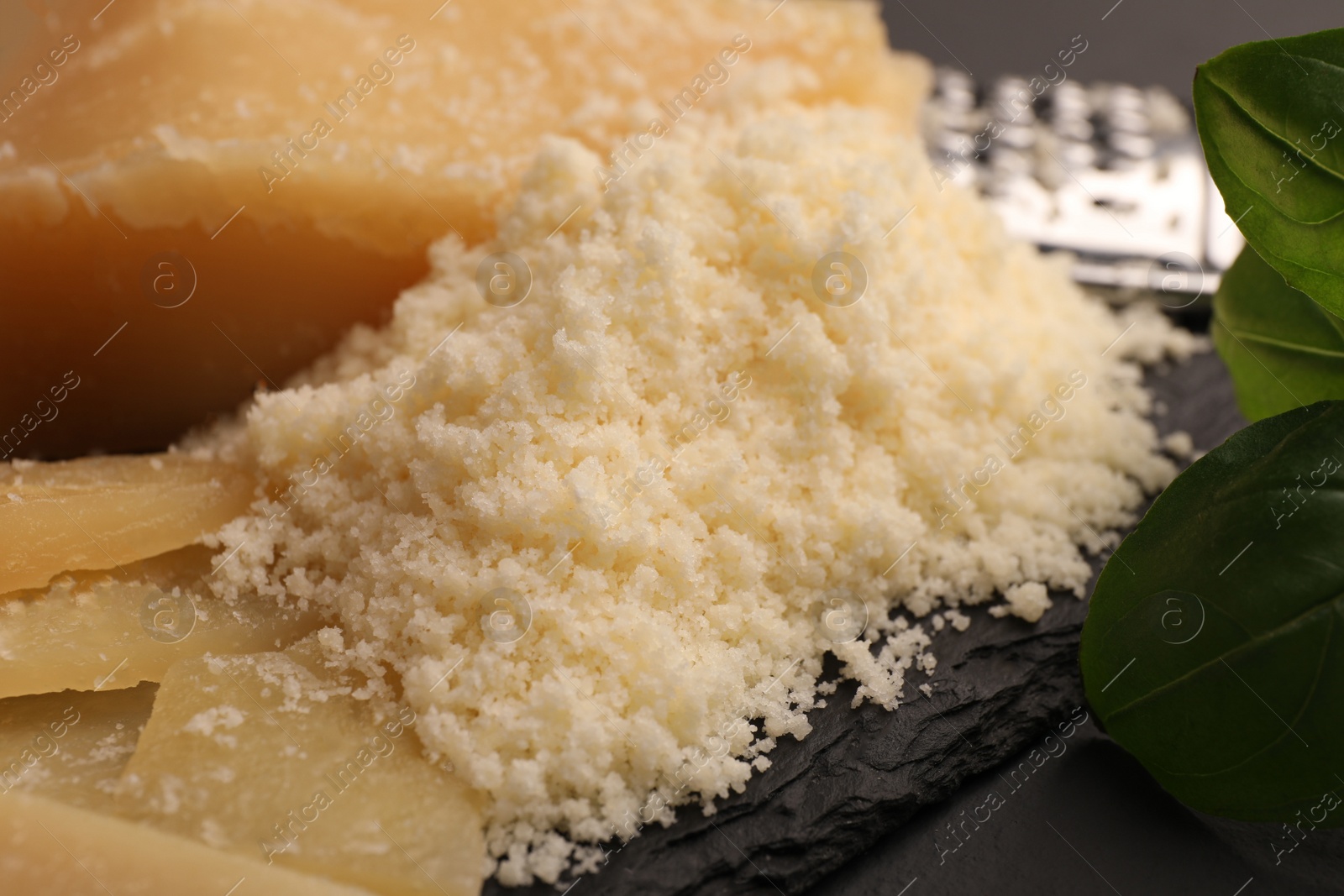 Photo of Delicious grated parmesan cheese on black slate board, closeup