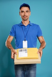 Photo of Happy young courier with parcel and envelopes on blue background