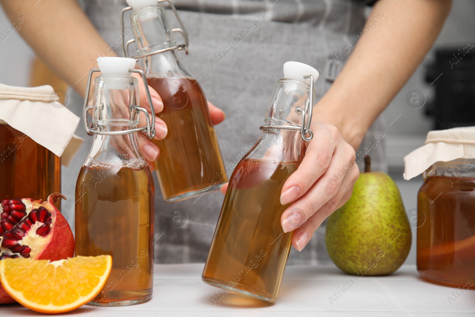 Photo of Woman taking bottles of fermented kombucha at white table, closeup