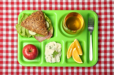 Photo of Serving tray with healthy food on tablecloth, top view. School lunch
