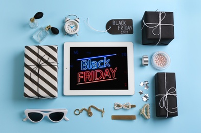 Photo of Flat lay composition with tablet, gifts and accessories on light blue background. Black Friday sale