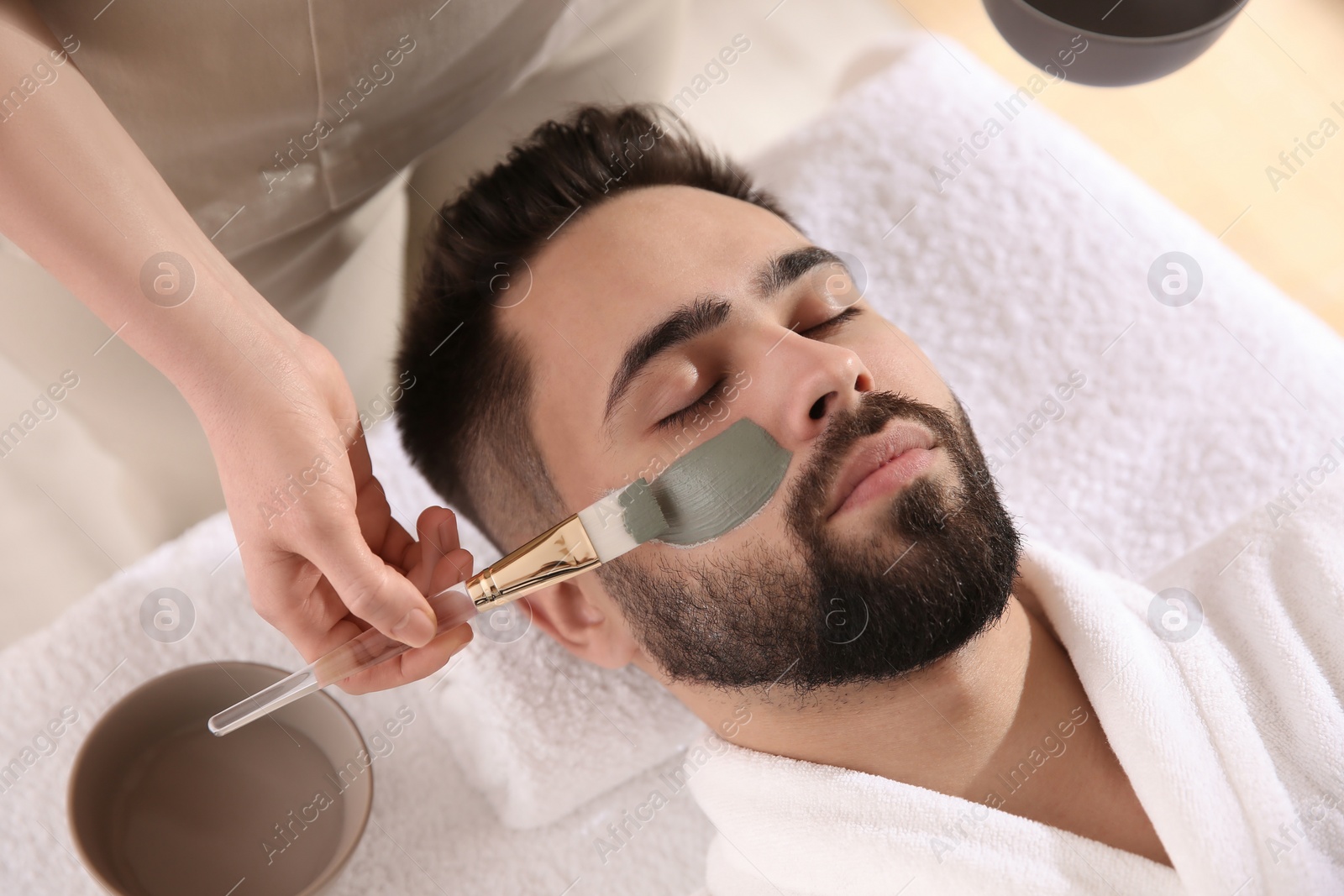 Photo of Cosmetologist applying mask on man's face in spa salon