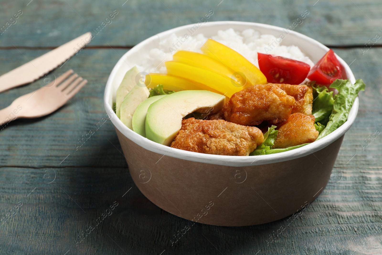 Photo of Healthy takeaway meal in paper container on blue wooden table