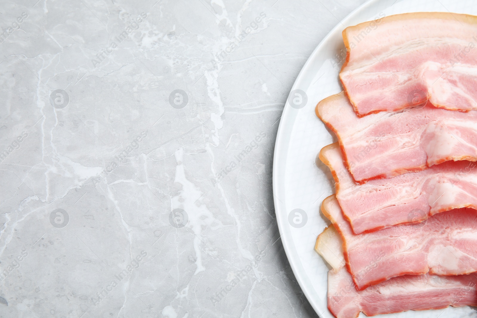 Photo of Plate of sliced raw bacon on light grey marble table, top view. Space for text