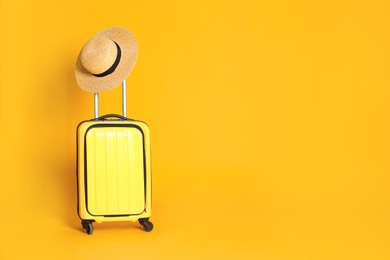 Travel suitcase with hat on yellow background, space for text. Summer vacation