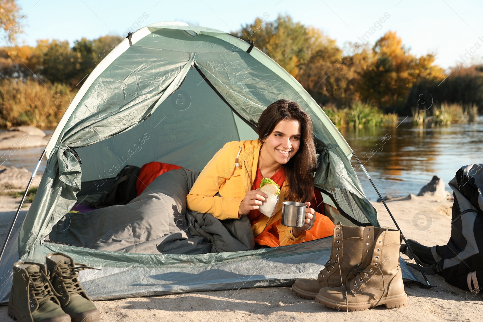 Photo of Young woman having breakfast in sleeping bag inside of camping tent
