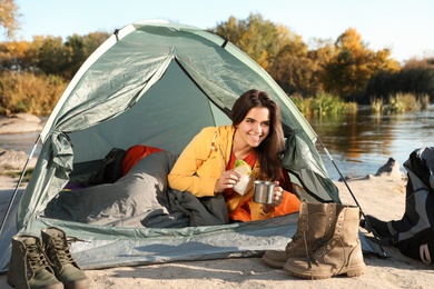 Young woman having breakfast in sleeping bag inside of camping tent