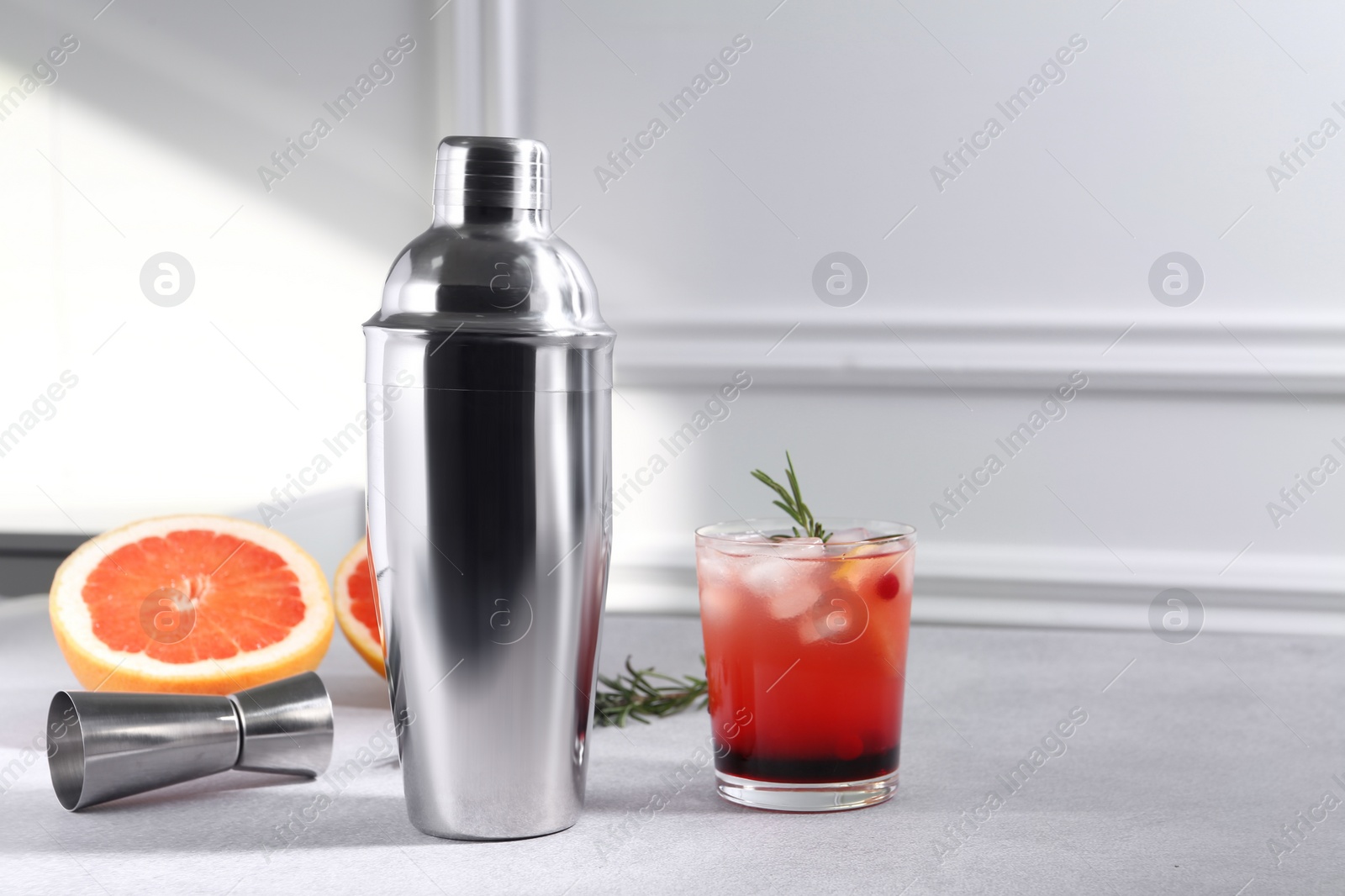 Photo of Metal shaker, delicious cocktail, jigger and grapefruit on light grey table, space for text