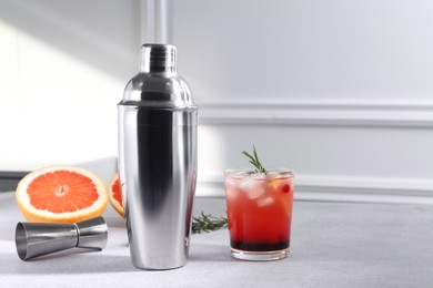 Metal shaker, delicious cocktail, jigger and grapefruit on light grey table, space for text