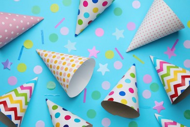 Photo of Bright party hats and confetti on light blue background, flat lay