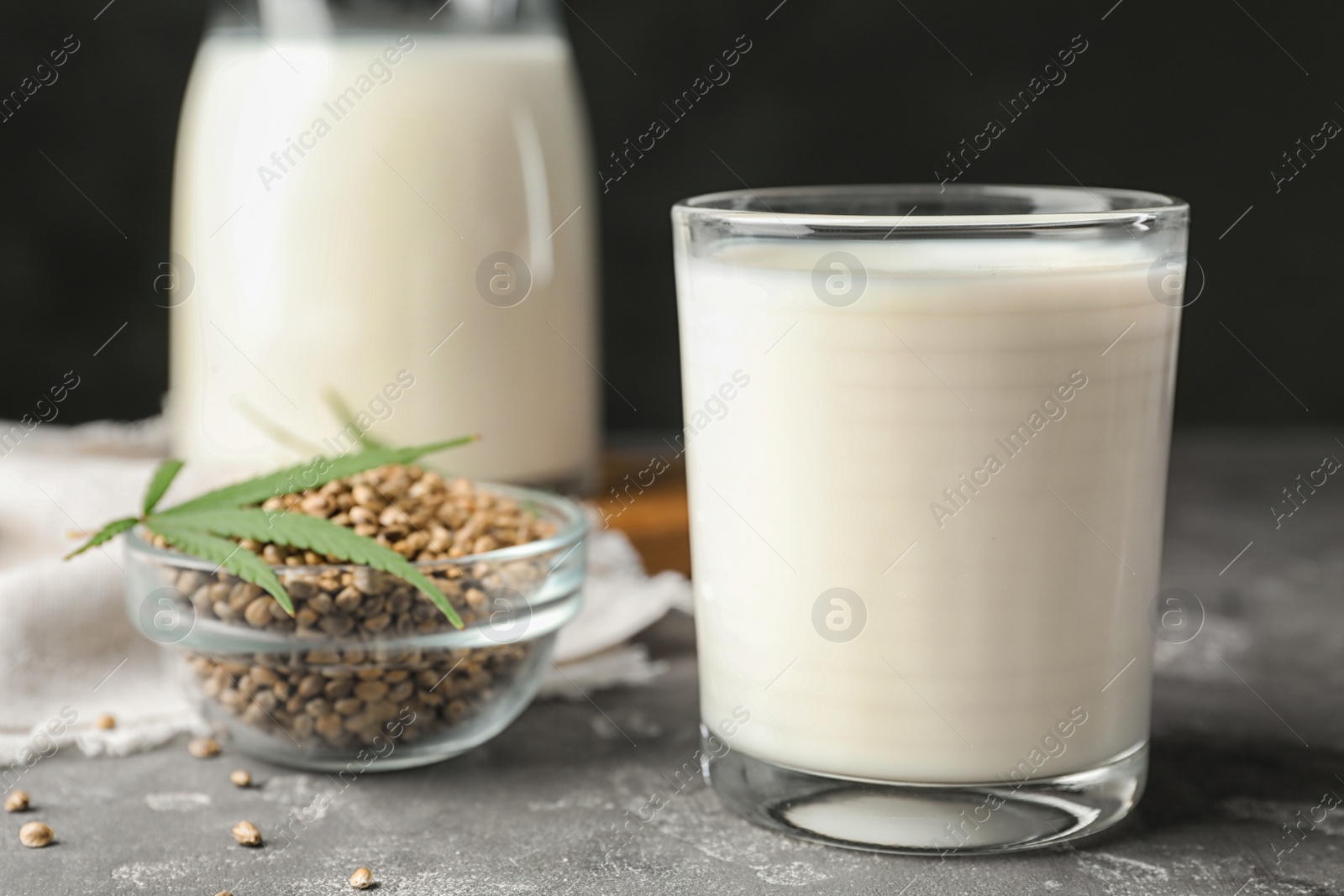 Photo of Composition with glass of hemp milk on grey table against black background, closeup