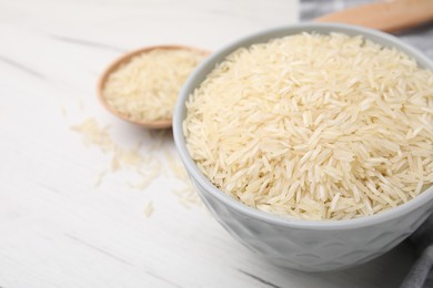 Raw rice in bowl on white wooden table, closeup. Space for text