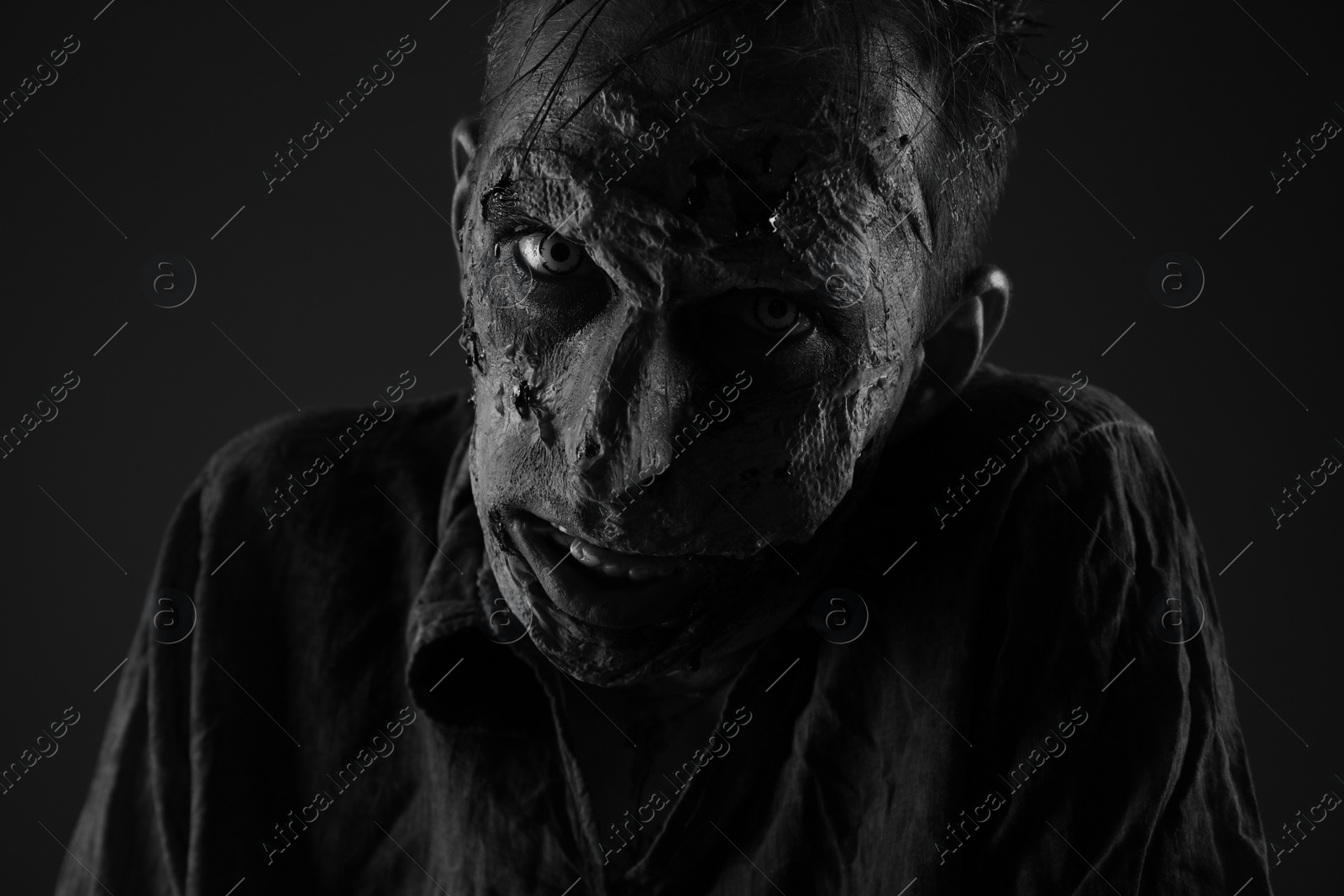 Photo of Scary zombie on dark background, black and white effect. Halloween monster