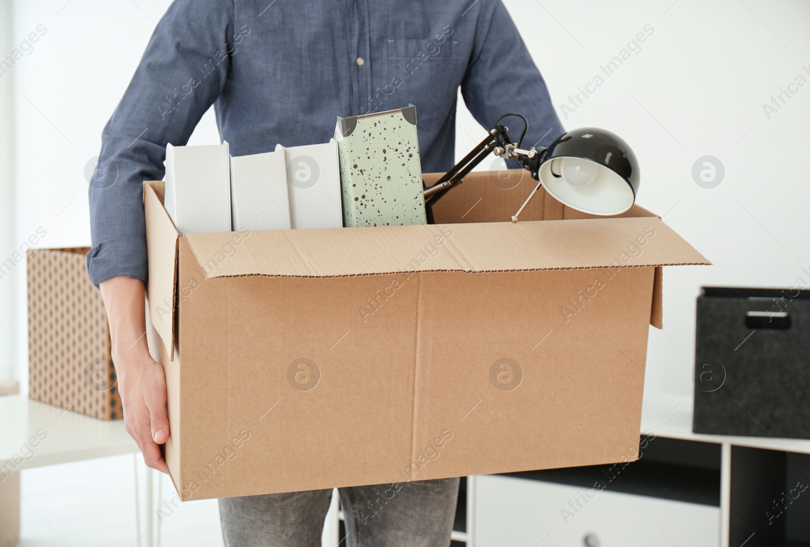 Photo of Young man holding moving box with office stuff indoors, closeup