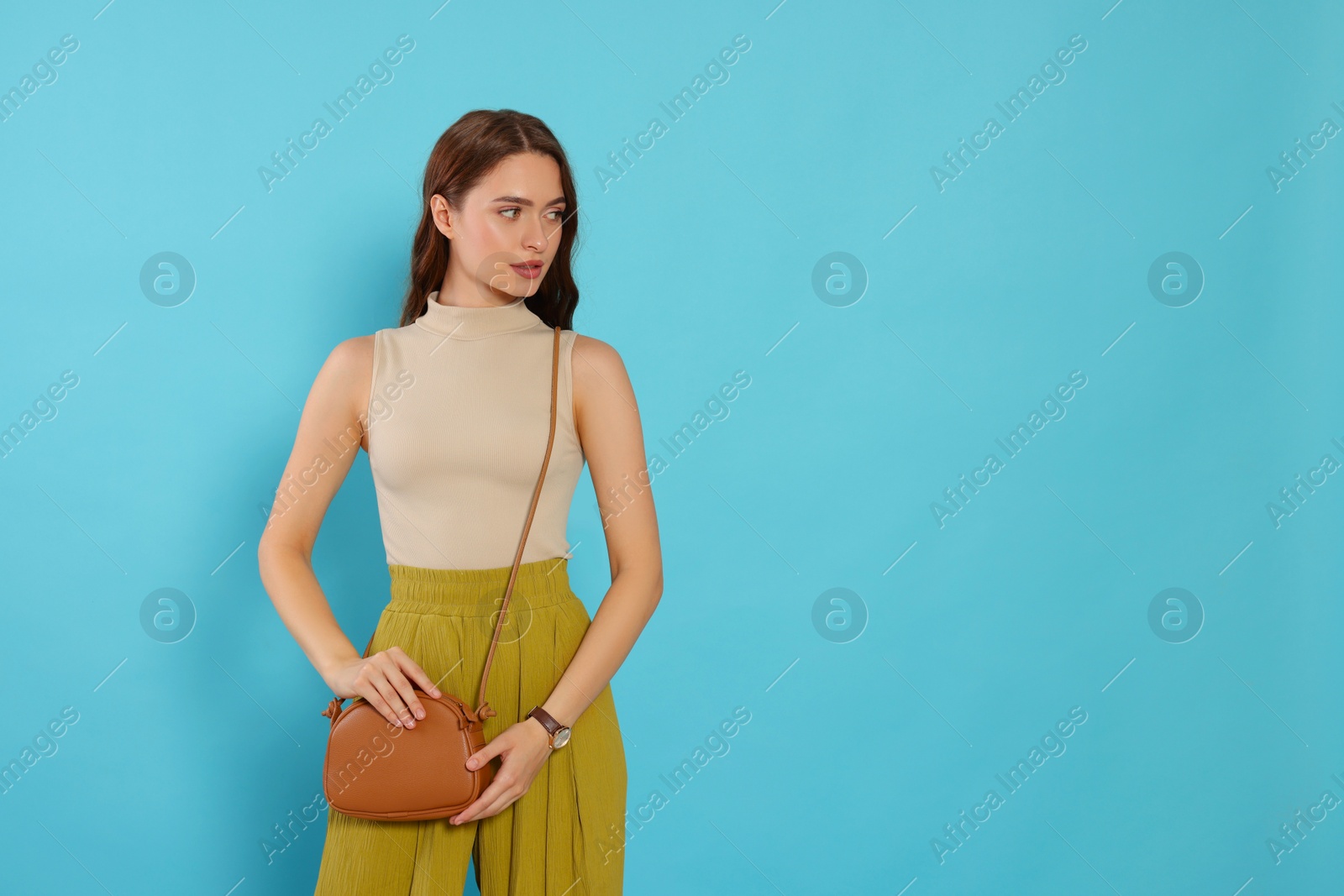 Photo of Beautiful young woman in fashionable outfit with stylish bag on light blue background, space for text