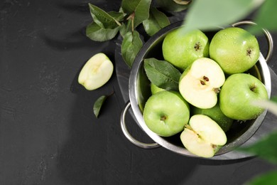 Ripe green apples with water drops and leaves on black table, flat lay. Space for text