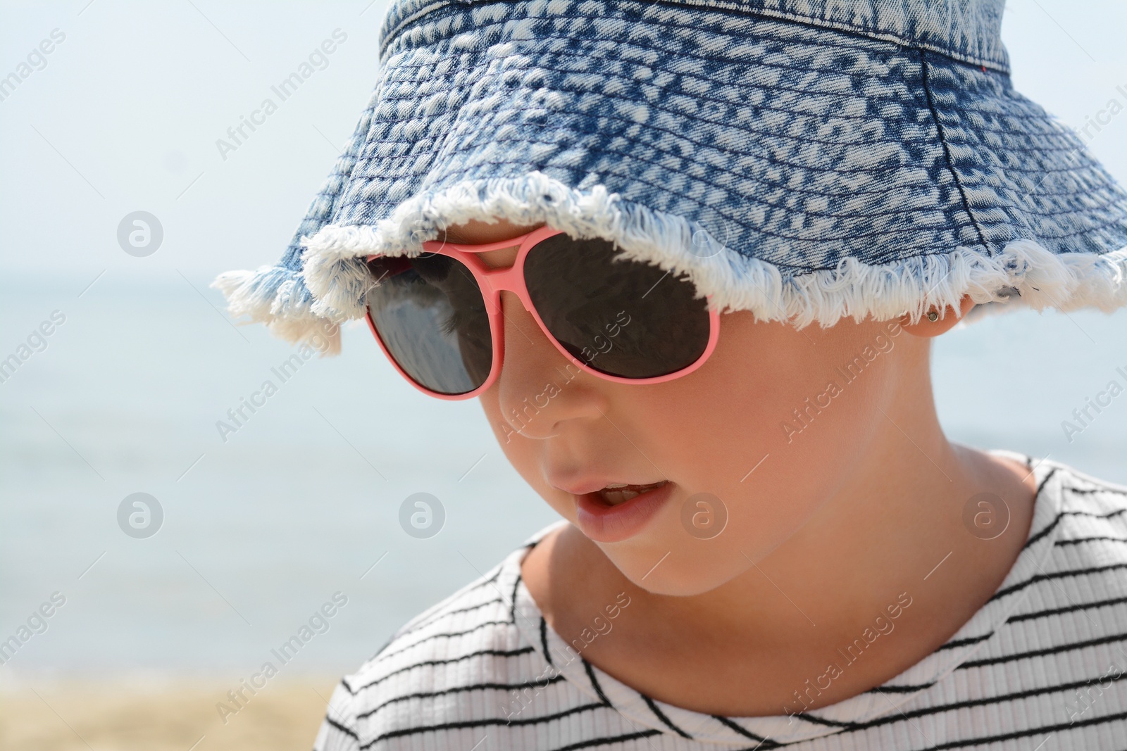 Photo of Little girl wearing sunglasses and hat at beach on sunny day