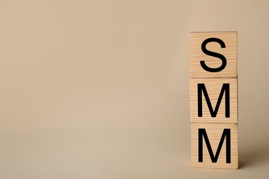 Photo of Wooden cubes with abbreviation SMM (Social media marketing) on beige background. Space for text