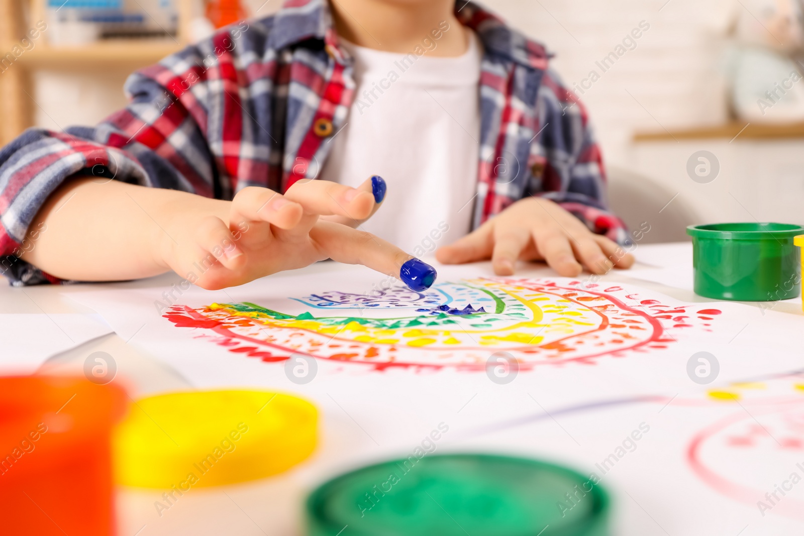 Photo of Little boy painting with finger at white table indoors, closeup