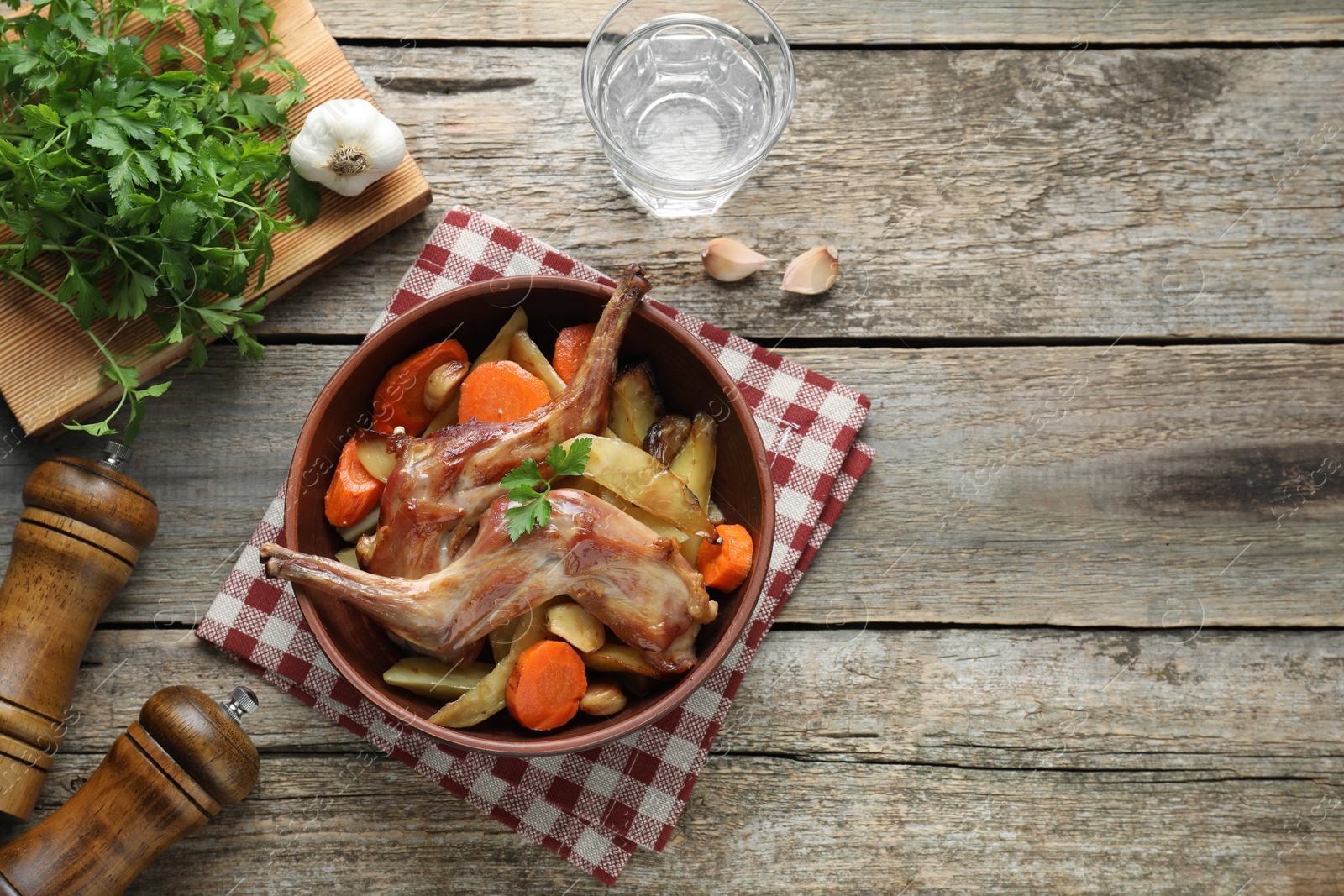 Photo of Tasty cooked rabbit with vegetables served on wooden table, flat lay. Space for text