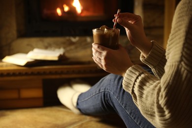 Woman with glass of hot cocoa near fireplace at home, closeup. Space for text