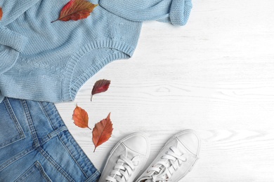 Photo of Stylish outfit and autumn leaves on white wooden background, flat lay with space for text. Trendy warm clothes