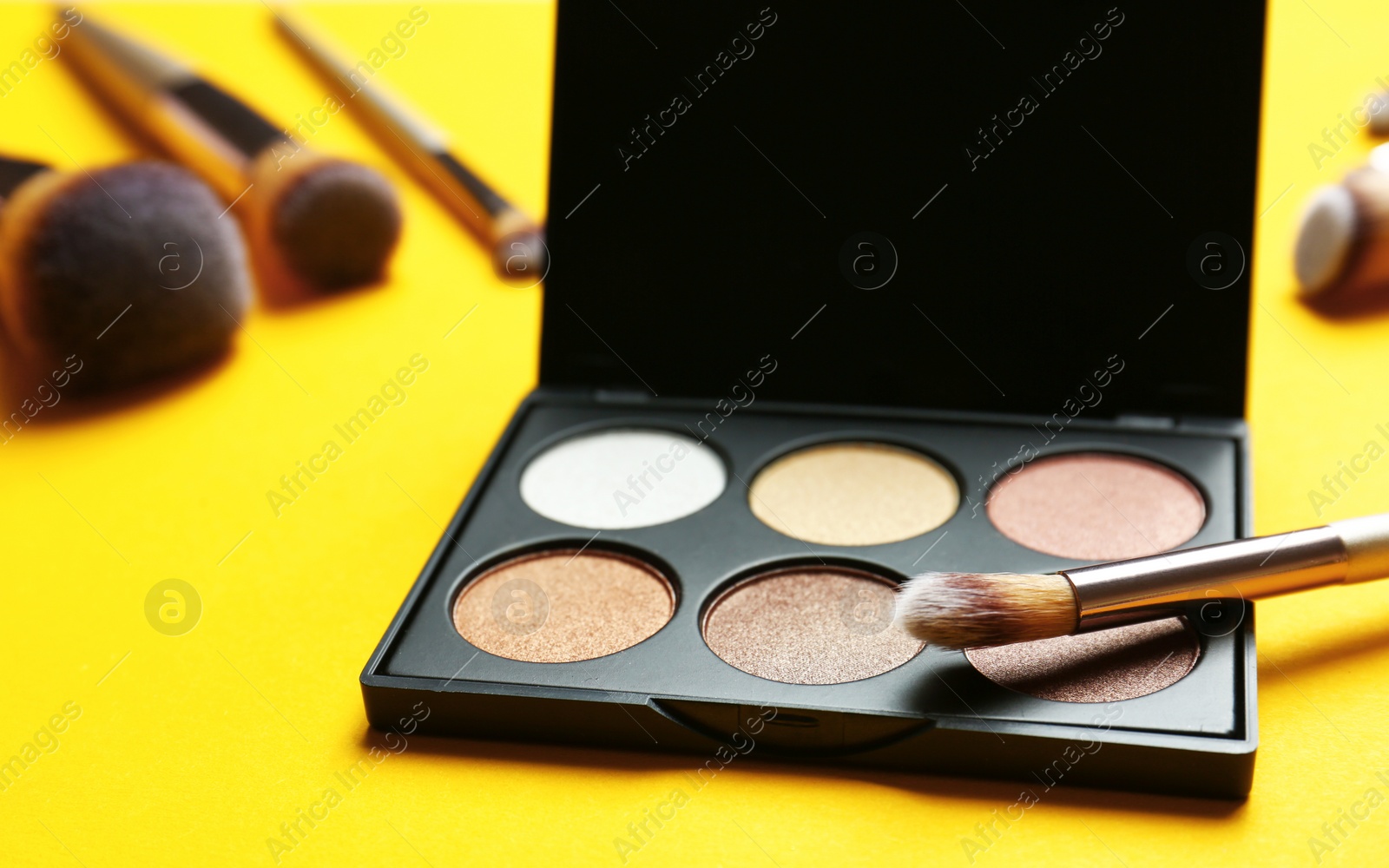 Photo of Eye shadow palette with professional makeup brush on yellow background